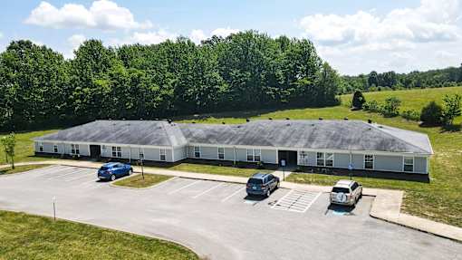 A large building with a grey roof and a parking lot in front.
