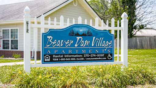 A sign for Beaver Dam Village Apartments is displayed in front of a house.