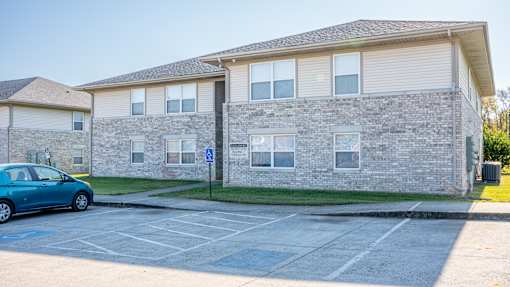 A blue car is parked in a parking lot in front of a building with a handicap sign.