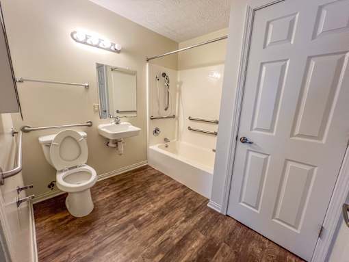 A white toilet is in a small bathroom with wood flooring.