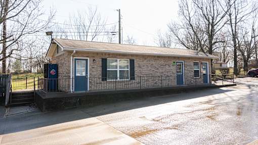 A small building with a blue door and windows is surrounded by a metal fence.