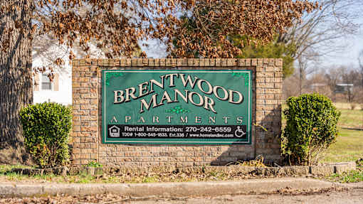 A sign for Brentwood Manor Apartments is displayed on a brick wall.