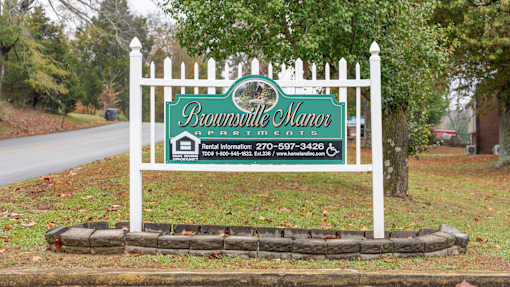 Brownville Manor sign with a white fence in front.
