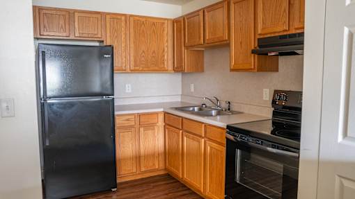 A black refrigerator sits in a kitchen with wooden cabinets.