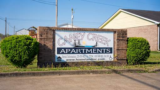 A sign for Caney Creek Apartments is displayed in front of a house.