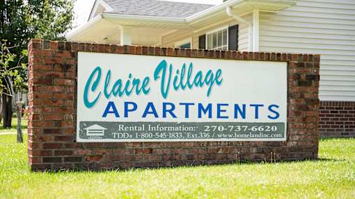 A sign for Claire Village Apartments with a phone number and website listed.