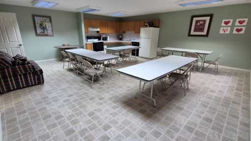 A room with tables and chairs and a kitchen in the background.