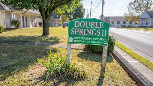 A sign for Double Springs II residential area stands in front of a tree.