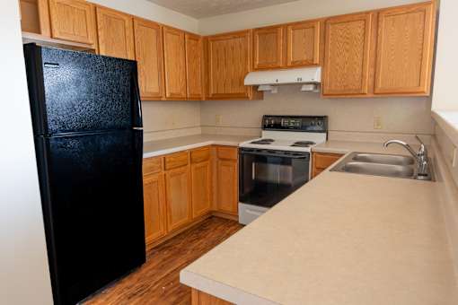 A black fridge stands next to a black oven in a kitchen with wooden cabinets.