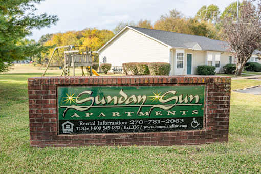 A sign for Sunday Sun Apartments with a playground in the background.