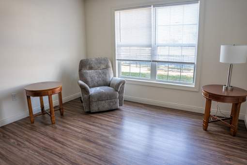 A grey armchair sits in a room with a wooden table and lamp.