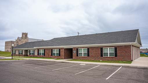 A parking lot in front of a brick building with a tower-like structure in the background.