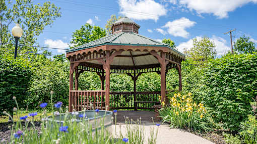 A gazebo surrounded by a garden with a pool in the middle.