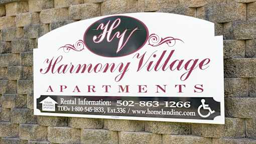 A sign for Harmony Village Apartments with a phone number and website listed.