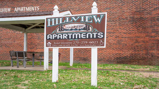 A sign for Hillyview Apartments is displayed in front of a brick building.