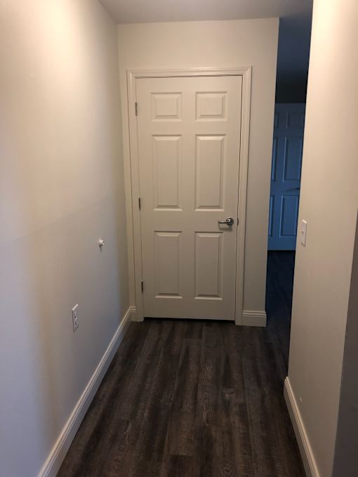 A white door is in a hallway with wood flooring.
