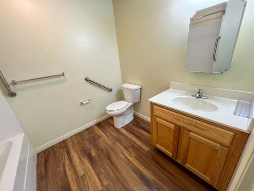 A small bathroom with wood flooring and a white toilet.