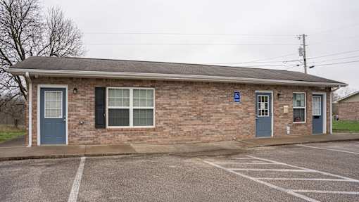 A small brick building with a blue door and a parking lot in front.