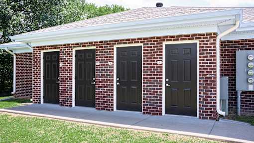 A red brick building with black doors and a grey electrical box on the side.