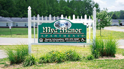A sign for Mya Manor Apartments with a phone number and website.