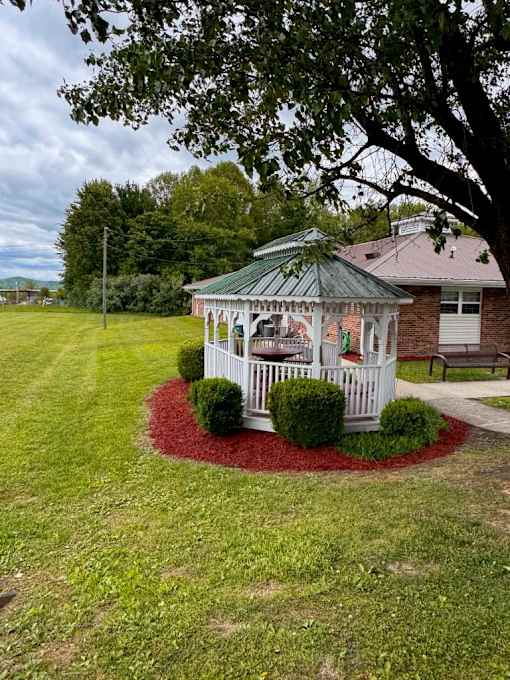 A gazebo is surrounded by a red mulch circle in a grassy yard.