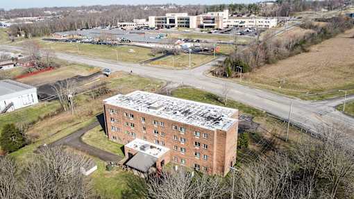 A large red brick building with a white roof is surrounded by a parking lot and other buildings.