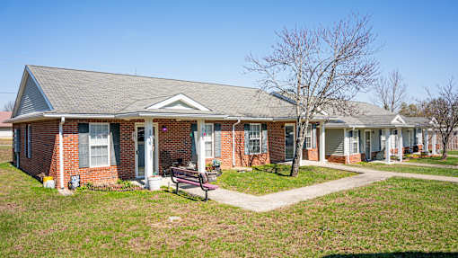A brick house with a porch and a bench in front.