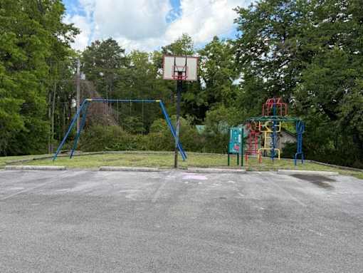 A basketball court with a hoop and a playground in the background.