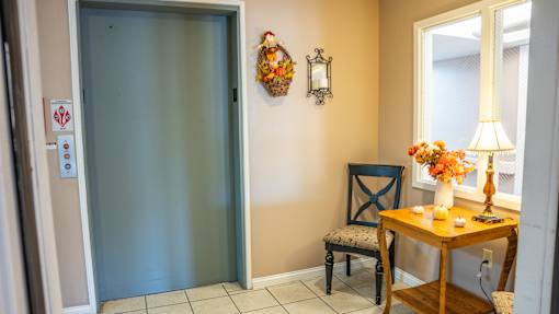 A room with a table, chair, and a wall-mounted light fixture.