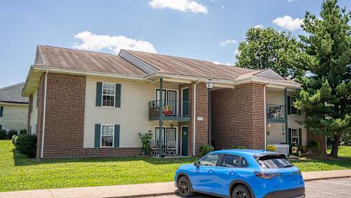 A blue car is parked in front of a two-story house.
