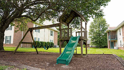 A playground with a green slide and a wooden swing set.
