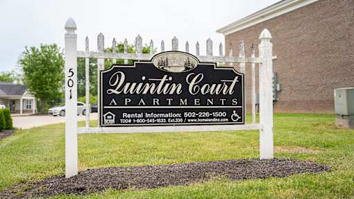 A sign for Quinton Court Apartments is displayed in front of a building.