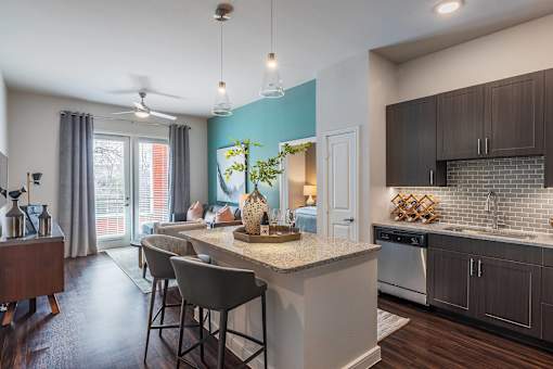 Luxury apartment kitchen with granite countertops, stainless steel appliances, tile backsplash, and oversized island with seating