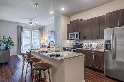 Luxury apartment kitchen with granite countertops, stainless steel appliances, tile backsplash, and oversized island with seating