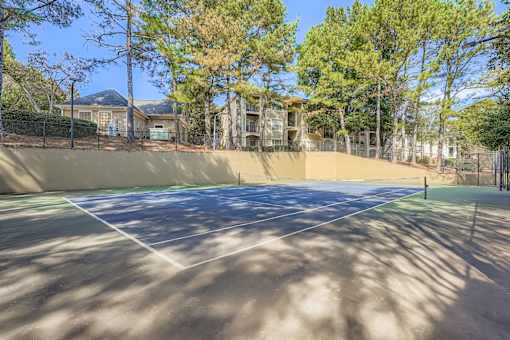 A tennis court surrounded by trees and apartment buildings.