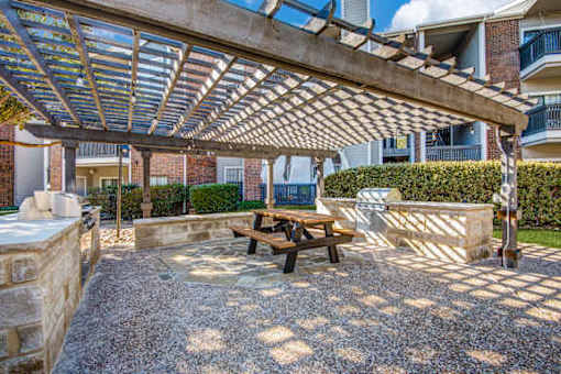A patio with a table and bench under a pergola.