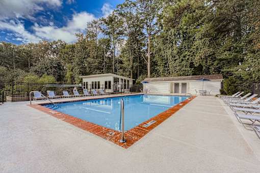 A large outdoor swimming pool surrounded by trees and lounge chairs.