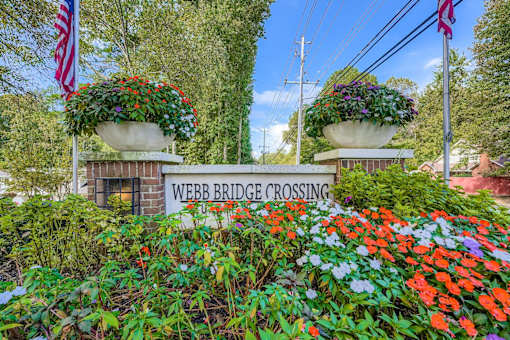 A sign that says Webb Bridge Crossing is surrounded by flowers.