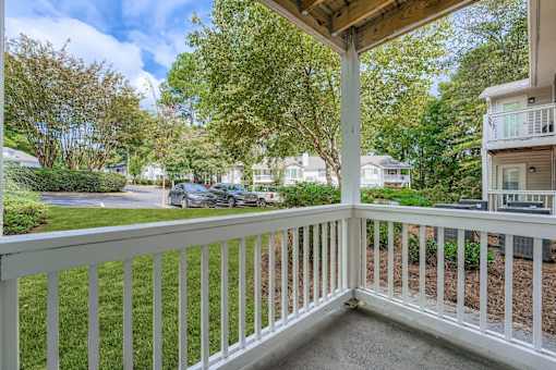 A white railing leads to a covered deck with a view of a tree-lined street.