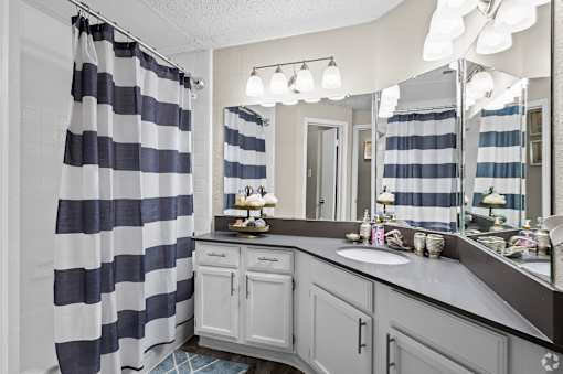 A bathroom with a striped shower curtain and a vanity with a mirror.