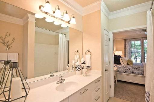 A bathroom with a large mirror, a sink, and a bedroom in the background.