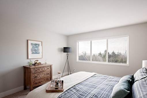 A bedroom with a bed, nightstand, and a window with blinds.
