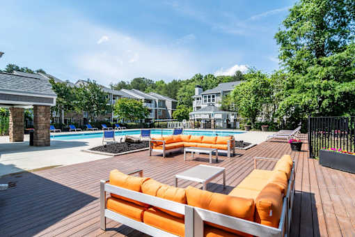 A wooden deck with orange cushions and a pool in the background.