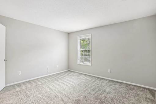 A room with a carpeted floor and a window with blinds.