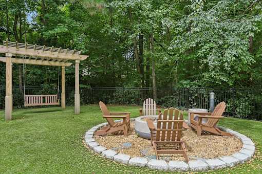 A wooden bench and chairs are arranged around a fire pit in a garden.