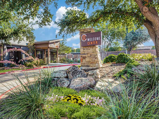 A welcome center sign is in front of a building with a landscaped area.