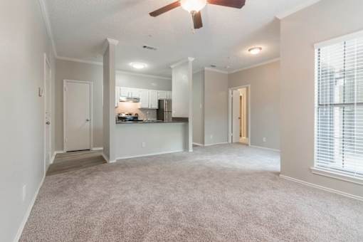 A spacious living room with a carpeted floor and a ceiling fan.