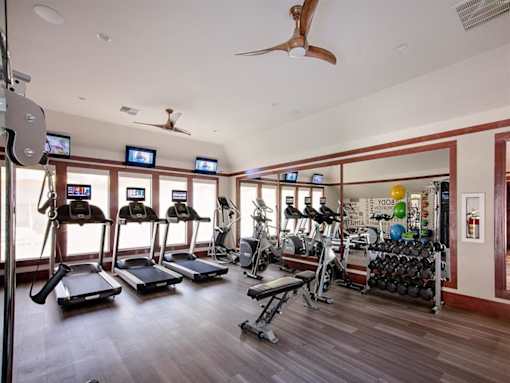 A gym with treadmills, exercise bikes, and a fan.
