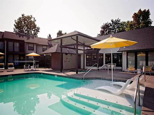 A pool with a yellow umbrella and white chairs.