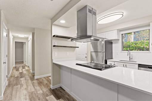 A modern kitchen with a stainless steel range hood and white countertops.